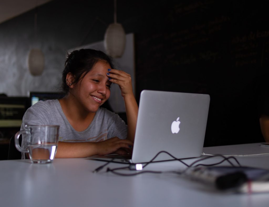 Una joven sonriendo frente a la pantalla de la computadora.